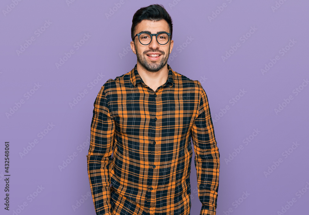 Hispanic man with beard wearing casual clothes and glasses looking positive and happy standing and smiling with a confident smile showing teeth Hispanic man with beard wearing casual clothes and glasses looking positive and happy standing and smiling with a confident smile showing teeth