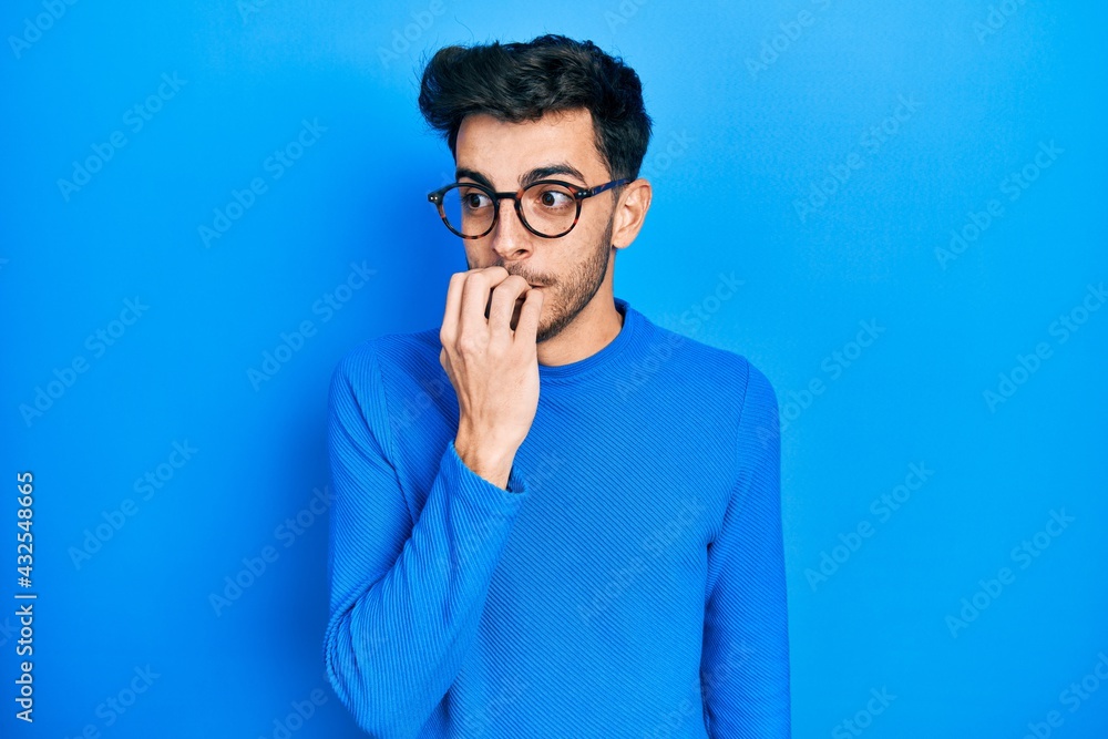 Young hispanic man wearing casual clothes and glasses looking stressed and nervous with hands on mouth biting nails. anxiety problem. Young hispanic man wearing casual clothes and glasses looking stressed and nervous with hands on mouth biting nails. anxiety problem.
