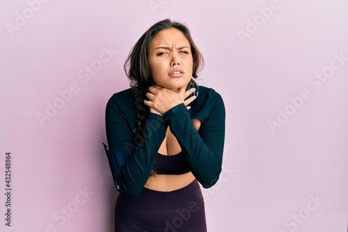 Young hispanic girl wearing sportswear and headphones shouting and suffocate because painful strangle. health problem. asphyxiate and suicide concept.