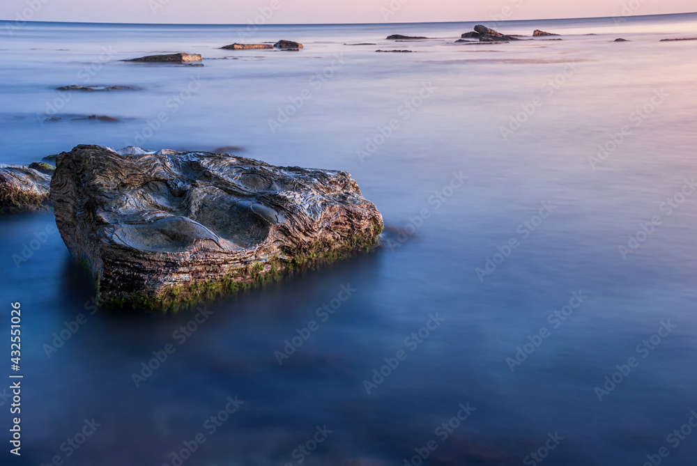Seascape at sunset. Sea on a long shutter with stones and rocks.