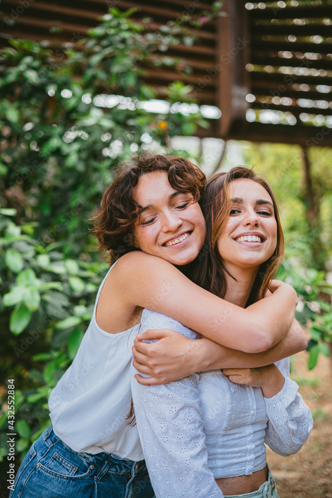 Two young teenager girls hugging each other and smiling surrounded by plants. They are having fun. Two young teenager girls hugging each other and smiling surrounded by plants. They are having fun.