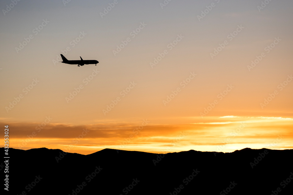 Silhouette of a jet plane over an orange sunrise over a mountain range