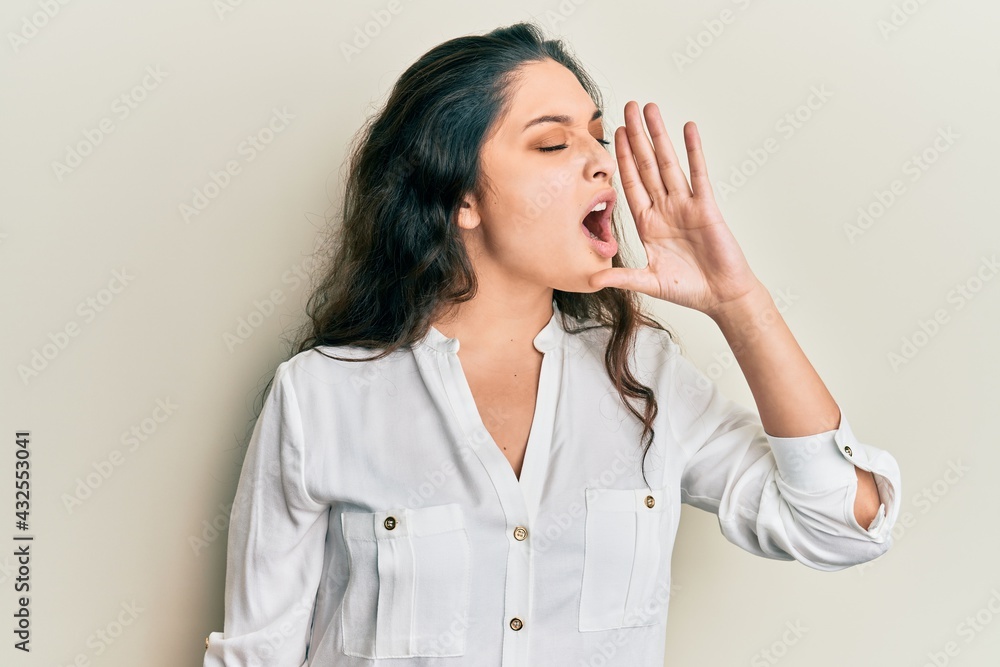 Beautiful middle eastern woman wearing casual clothes shouting and screaming loud to side with hand on mouth. communication concept. Beautiful middle eastern woman wearing casual clothes shouting and screaming loud to side with hand on mouth. communication concept.