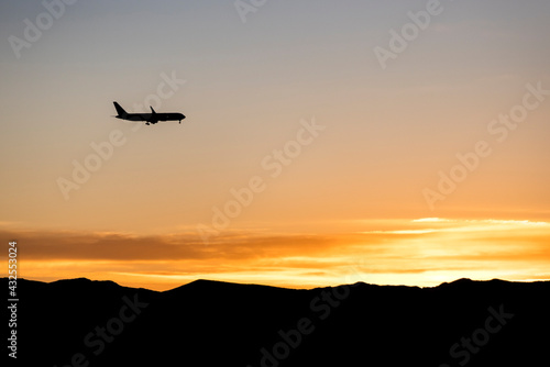 Silhouette of a jet plane over an orange sunrise over a mountain range