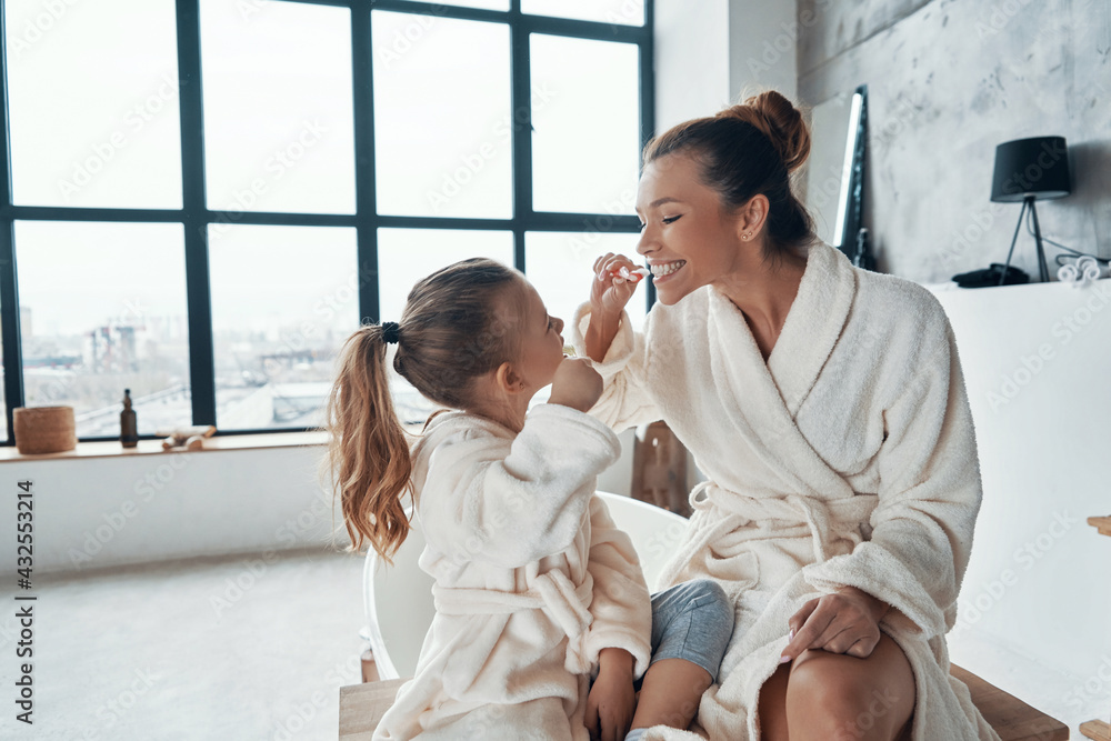 Mother and daughter in bathrobes smiling and cleaning teeth Mother and daughter in bathrobes smiling and cleaning teeth