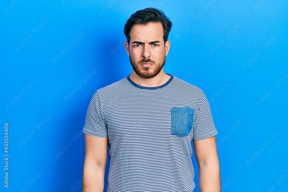 Handsome caucasian man with beard wearing casual striped t shirt skeptic and nervous, frowning upset because of problem. negative person. Handsome caucasian man with beard wearing casual striped t shirt skeptic and nervous, frowning upset because of problem. negative person.