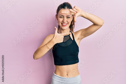 Young brunette woman wearing sportswear smiling making frame with hands and fingers with happy face. creativity and photography concept.
