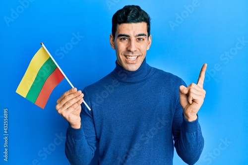 Handsome hispanic man holding lithuania flag smiling happy pointing with hand and finger to the side