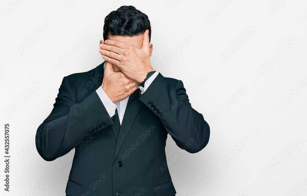 Handsome hispanic man wearing business clothes covering eyes and mouth with hands, surprised and shocked. hiding emotion Handsome hispanic man wearing business clothes covering eyes and mouth with hands, surprised and shocked. hiding emotion