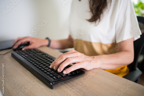 Close up of a woman working at home. Hands on the keyboard and a clean desk