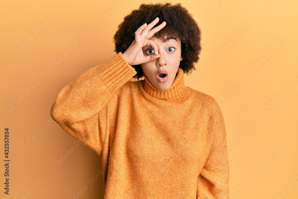 Young hispanic girl wearing wool winter sweater doing ok gesture shocked with surprised face, eye looking through fingers. unbelieving expression. Young hispanic girl wearing wool winter sweater doing ok gesture shocked with surprised face, eye looking through fingers. unbelieving expression.