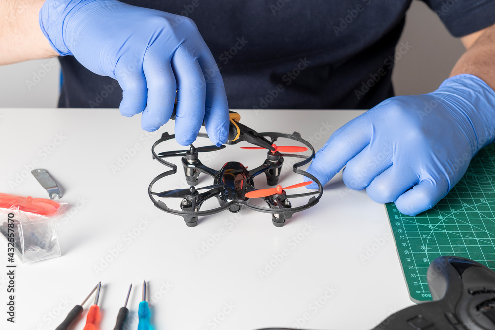 Man repairing the elices of a toy drone, various tools and spare parts of the drone on a table. View of the hands repairing Man repairing the elices of a toy drone, various tools and spare parts of the drone on a table. View of the hands repairing