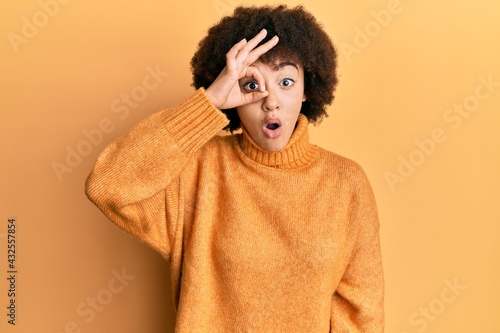 Young hispanic girl wearing wool winter sweater doing ok gesture shocked with surprised face, eye looking through fingers. unbelieving expression. © Krakenimages.com