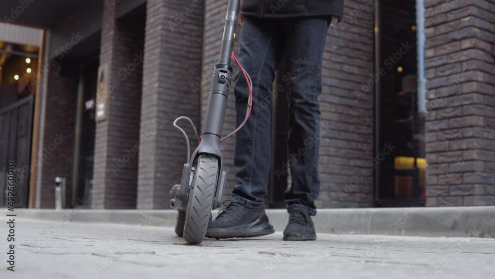 Young african american in black sweater and black jeans on the background. An electric scooter is in the foreground Young african american in black sweater and black jeans on the background. An electric scooter is in the foreground