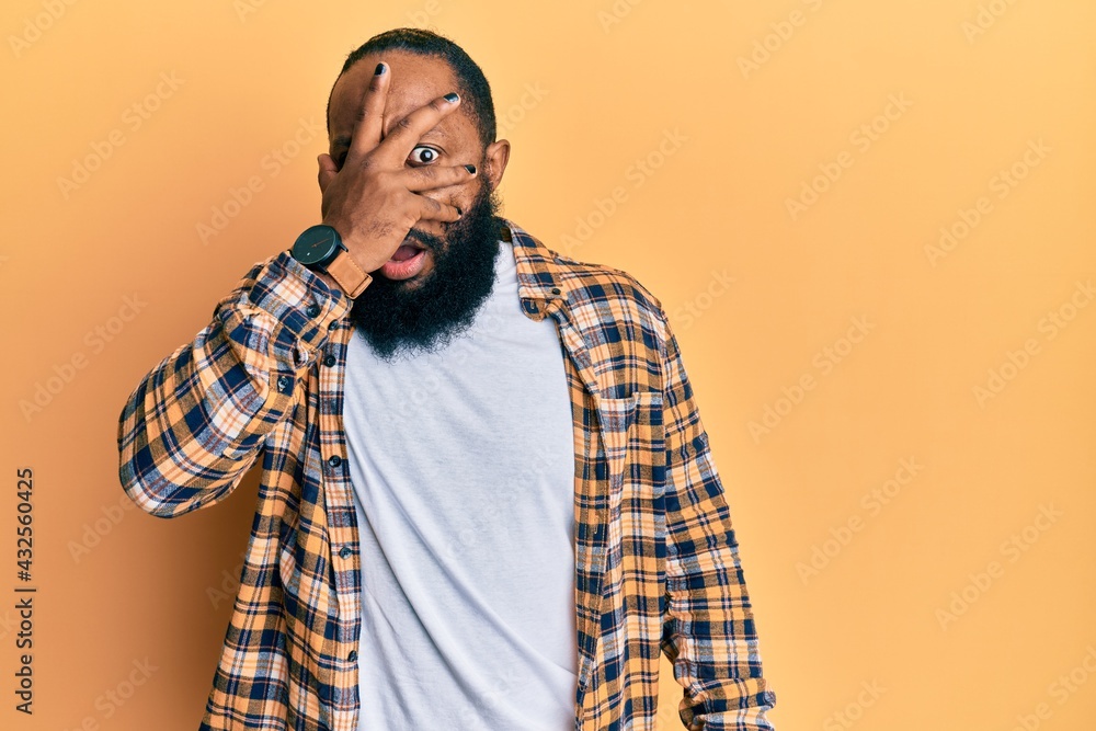 Young african american man wearing casual clothes peeking in shock covering face and eyes with hand, looking through fingers afraid Young african american man wearing casual clothes peeking in shock covering face and eyes with hand, looking through fingers afraid