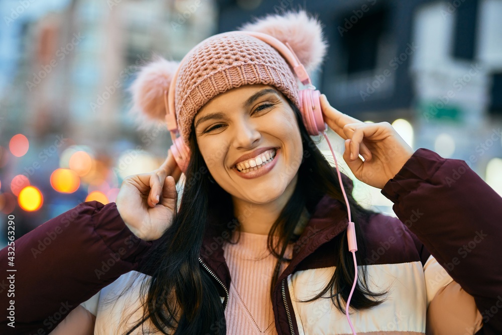 Young hispanic girl smiling happy using headphones at the city.