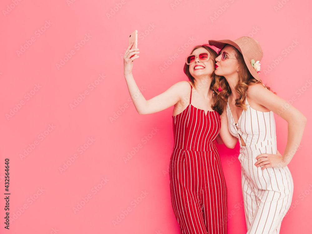Two young beautiful smiling hipster female in trendy summer overalls clothes. Sexy carefree women posing near pink wall in studio. Trendy and positive models having fun. Taking selfie photos Two young beautiful smiling hipster female in trendy summer overalls clothes. Sexy carefree women posing near pink wall in studio. Trendy and positive models having fun. Taking selfie photos