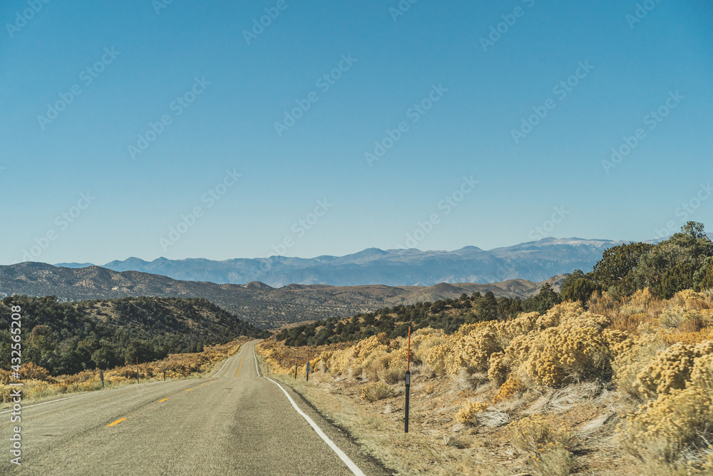 Two lane road in the arid Sierra Nevada's leading to mountains against blue sky