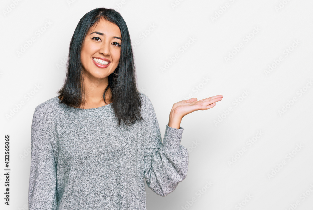 Beautiful asian young woman wearing casual clothes smiling cheerful presenting and pointing with palm of hand looking at the camera. Beautiful asian young woman wearing casual clothes smiling cheerful presenting and pointing with palm of hand looking at the camera.