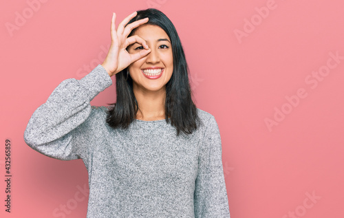 Beautiful asian young woman wearing casual clothes doing ok gesture with hand smiling, eye looking through fingers with happy face. © Krakenimages.com