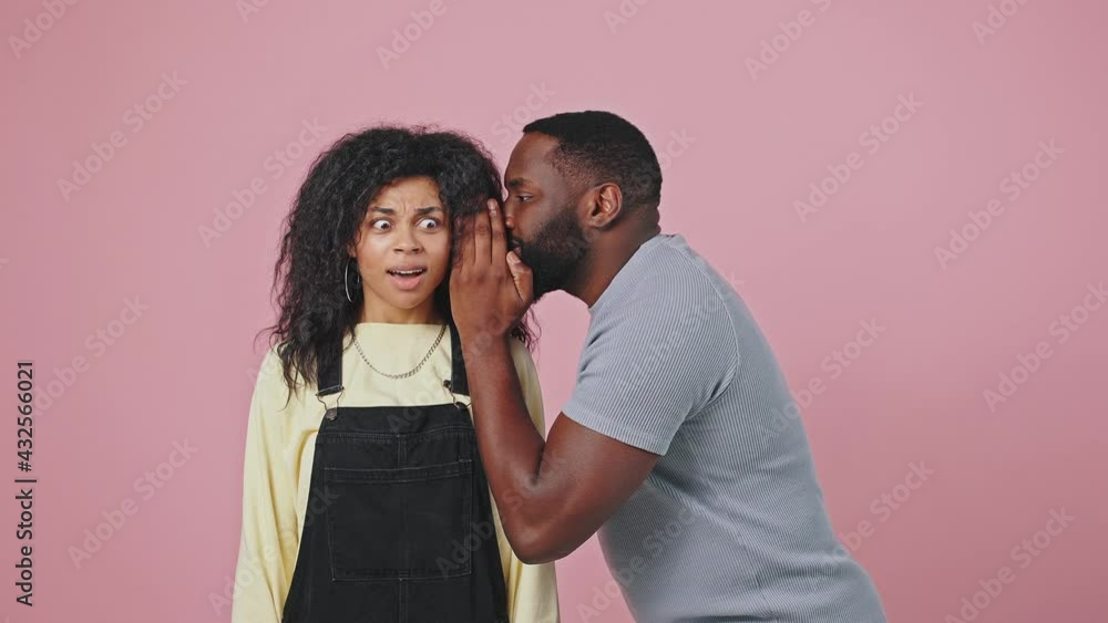 African american man coming to his girlfriend and whispering secret to her ear, woman feeling shock and amazement African american man coming to his girlfriend and whispering secret to her ear, woman feeling shock and amazement