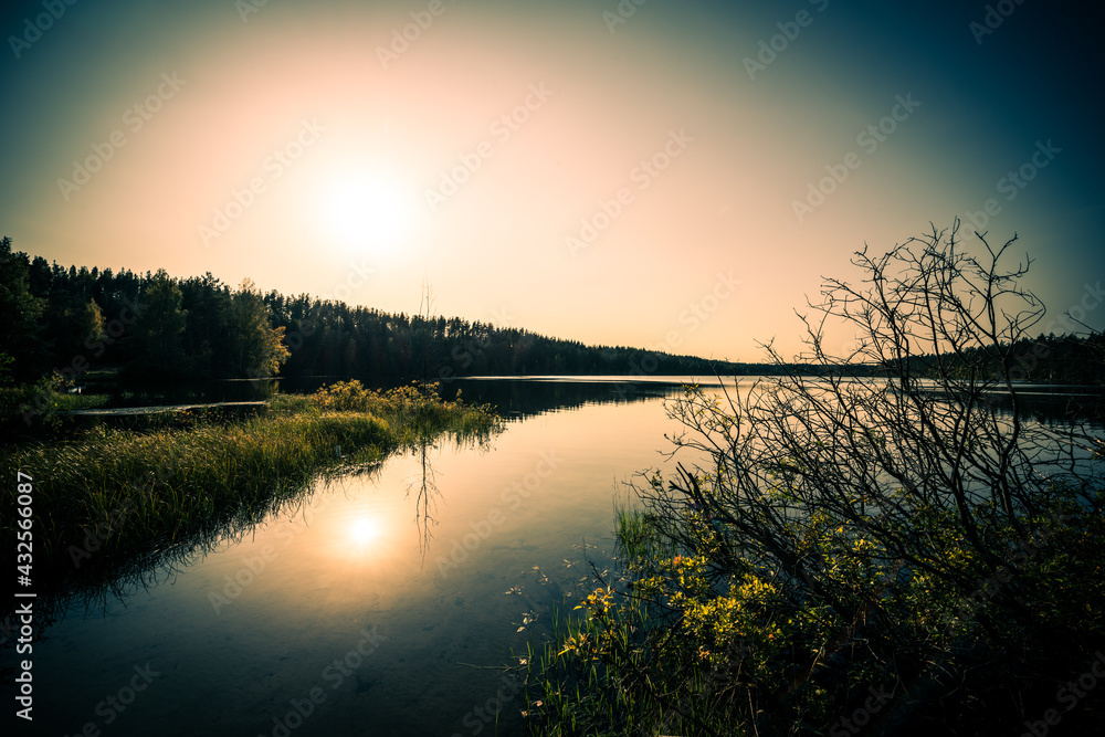 Obraz premium Sunset over the forest lake. View from the shore level, image vignetting and the orange-blue toning