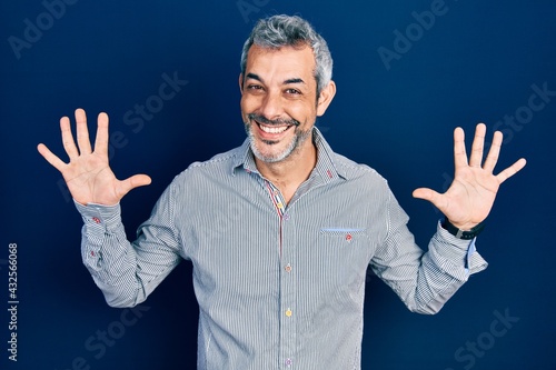 Handsome middle age man with grey hair wearing business shirt showing and pointing up with fingers number ten while smiling confident and happy.