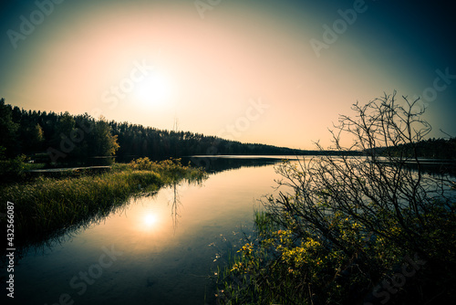 Sunset over the forest lake. View from the shore level, image vignetting and the orange-blue toning