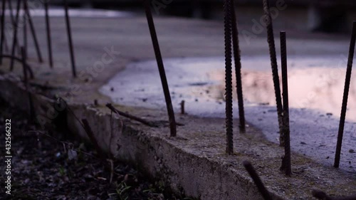 Closeup of metal fittings protrude from the concrete slabs of an abandoned building against the background of puddles and sunset