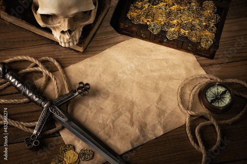 Pirate captain table with crumpled paper page with copy space for text. Compass, skull, gold coins, chest and dagger. Adventurer or pirate concept background.