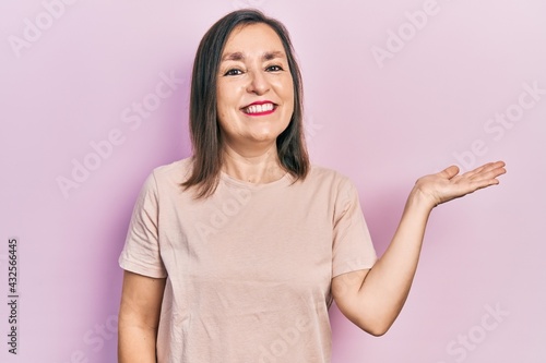 Middle age hispanic woman wearing casual clothes smiling cheerful presenting and pointing with palm of hand looking at the camera. © Krakenimages.com