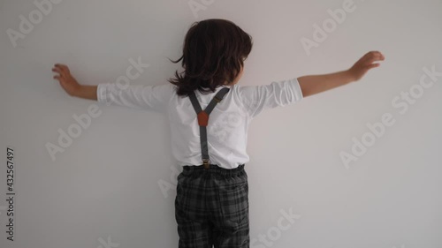 boy in a white T-shirt stands with his back to the white wal