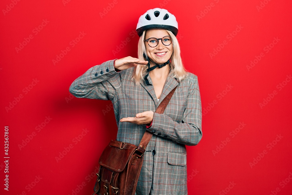 Beautiful caucasian blonde business woman wearing bike helmet gesturing with hands showing big and large size sign, measure symbol. smiling looking at the camera. measuring concept.
