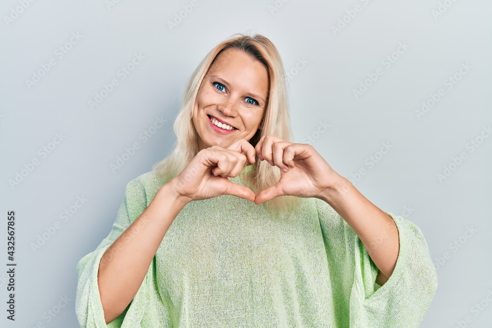 Beautiful caucasian blonde woman wearing casual winter sweater smiling in love doing heart symbol shape with hands. romantic concept. Beautiful caucasian blonde woman wearing casual winter sweater smiling in love doing heart symbol shape with hands. romantic concept.