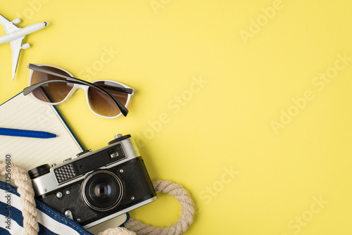 Above photo of sunglasses airplane bag camera notebook and blue pen isolated on the yellow background with blank space