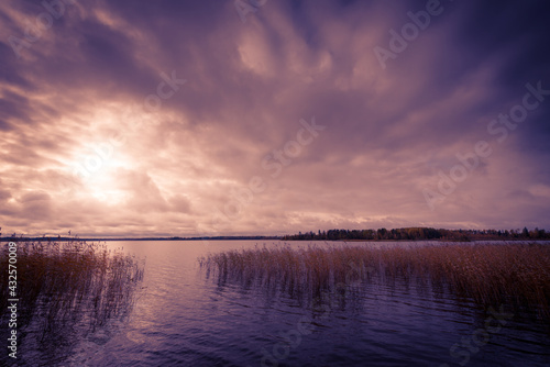Sunset in the cloudy sky over the autumn forest lake. Image vignetting and the orange-purple toning