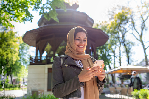 Muslim woman with hijab typing on her phone outside. 