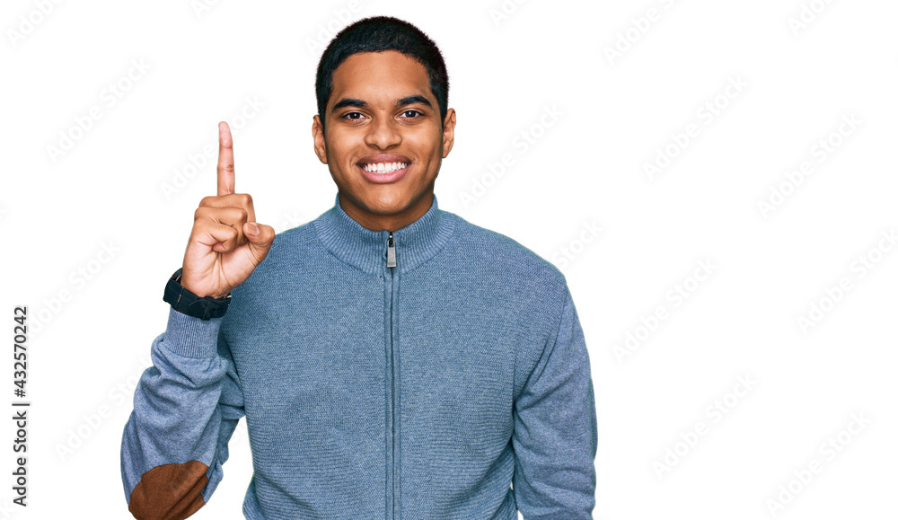 Young handsome hispanic man wearing casual sweatshirt showing and pointing up with finger number one while smiling confident and happy. Young handsome hispanic man wearing casual sweatshirt showing and pointing up with finger number one while smiling confident and happy.