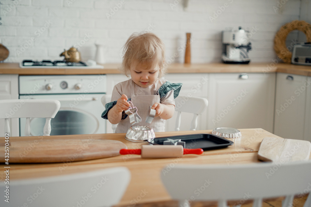An interesting activity for the baby. A child is playing in the kitchen with cake pans. Happy children's mood. Girl cook eats baked goods cookies, dessert confectionery. An interesting activity for the baby. A child is playing in the kitchen with cake pans. Happy children's mood. Girl cook eats baked goods cookies, dessert confectionery.