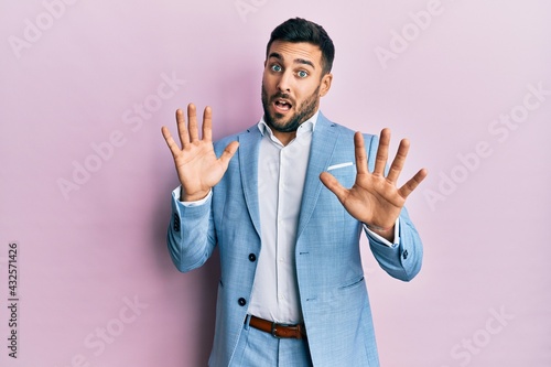 Young hispanic businessman wearing business jacket afraid and terrified with fear expression stop gesture with hands, shouting in shock. panic concept. © Krakenimages.com