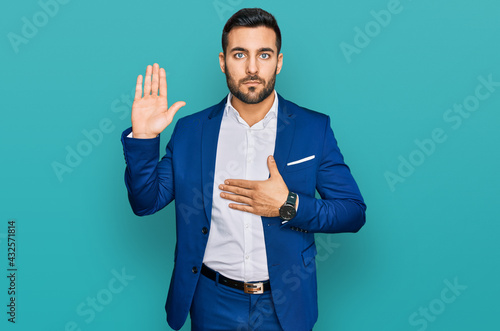 фотографія Young hispanic man wearing business jacket swearing with hand on chest and open