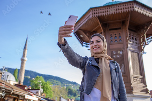 Muslim woman with hijab is taking selfie in front of the Sebilj in Sarajevo.  photo