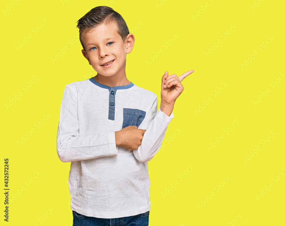 Adorable caucasian kid wearing casual clothes with a big smile on face, pointing with hand and finger to the side looking at the camera. Adorable caucasian kid wearing casual clothes with a big smile on face, pointing with hand and finger to the side looking at the camera.