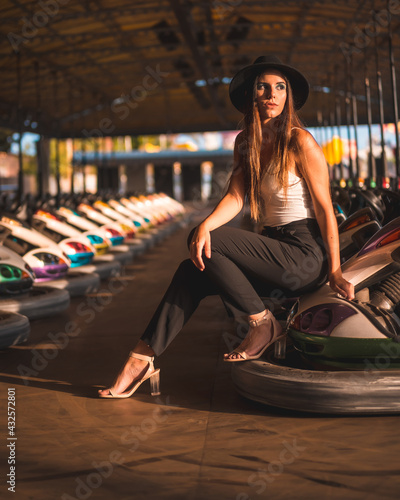 Lifestyle, Caucasian brunette with.long pants, white t-shirt and black hat in an amusement park in the bumper cars