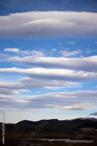 Portrait orientation three quarters of a sky filled with lenticular clouds over desert town and small pond by carson city