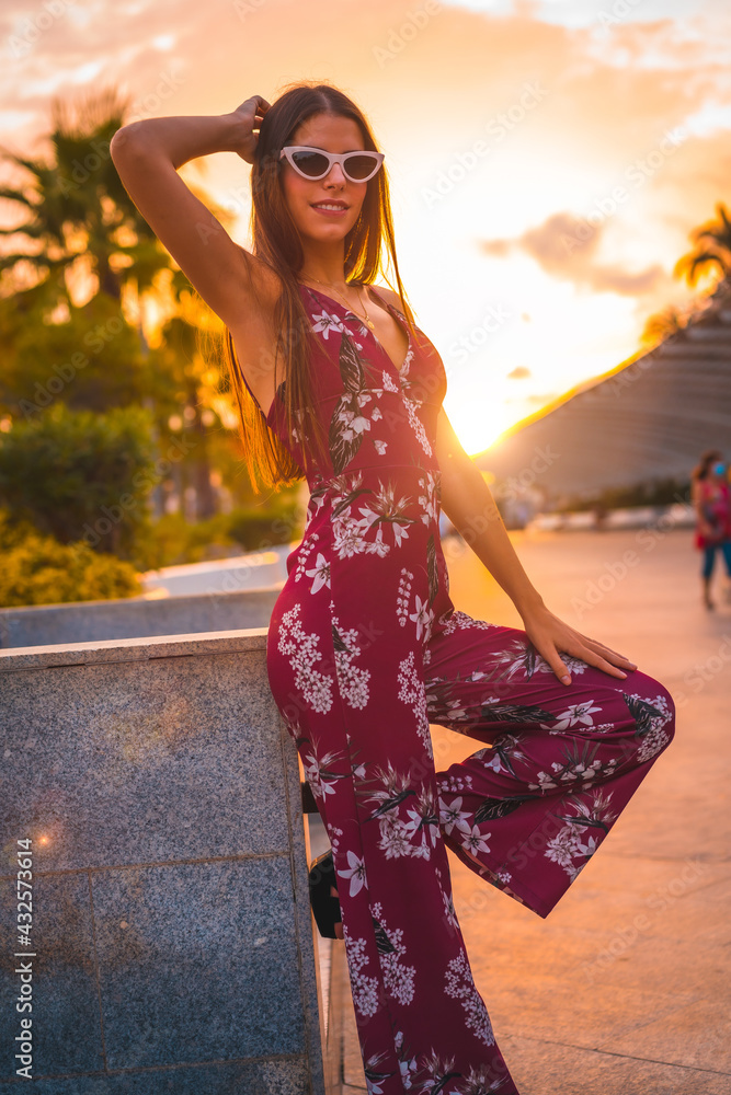 Street Style, sunset with a young brunette in a maroon floral dress and modern white sunglasses enjoying the summer in the golden hour