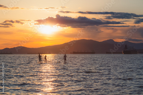 Silhouette of paddle boarders during sunset golden hour light on on open Pacific ocean water at Kitsilano Beach on an idyllic summer evening in Vancouver  B.C.  Canada.