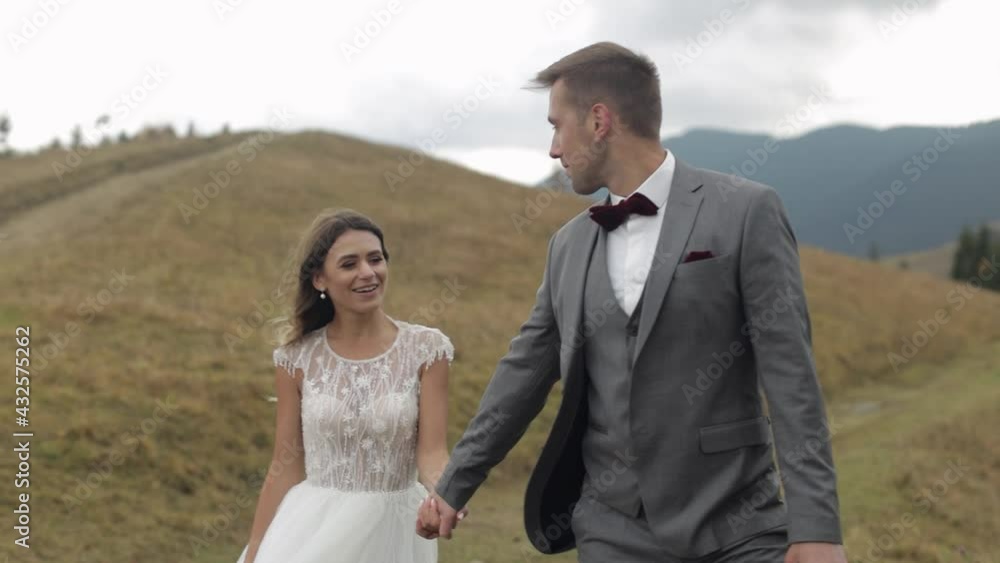 Lovely young caucasian newlyweds bride and groom walking on mountain slope hill. Wedding couple. Happy family. Man and woman in love. Autumn. Bride in gorgeous wedding dress. Cloudy sky background Lovely young caucasian newlyweds bride and groom walking on mountain slope hill. Wedding couple. Happy family. Man and woman in love. Autumn. Bride in gorgeous wedding dress. Cloudy sky background