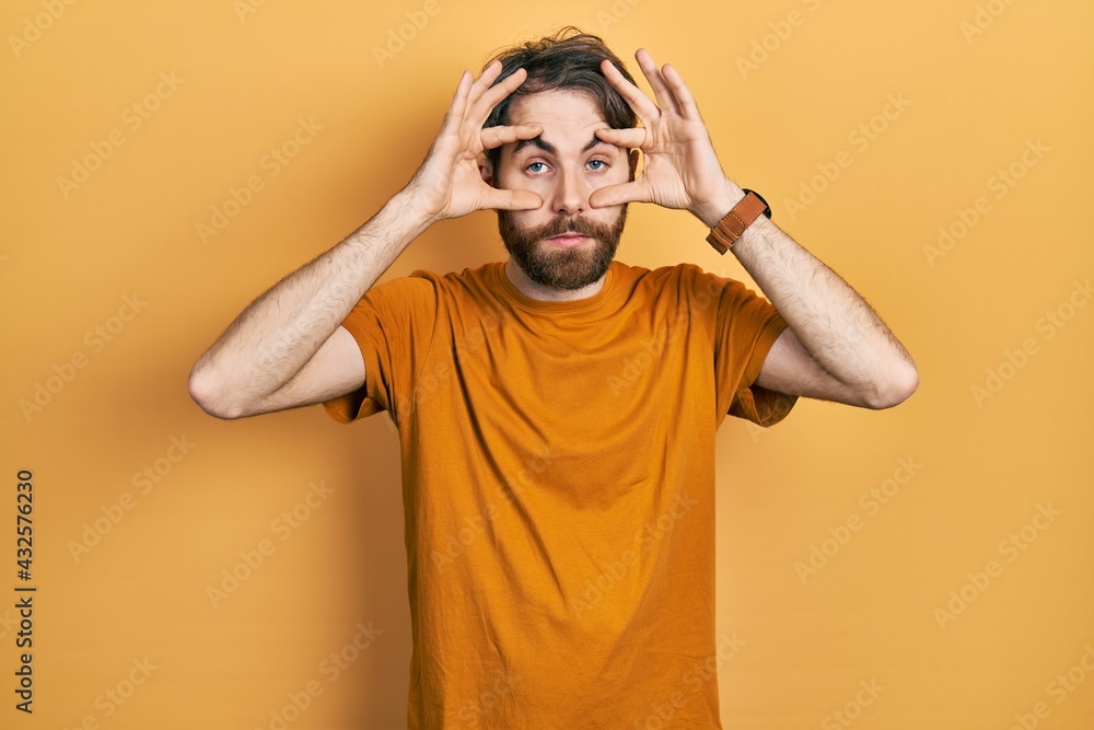 Caucasian man with beard wearing casual yellow t shirt trying to open eyes with fingers, sleepy and tired for morning fatigue Caucasian man with beard wearing casual yellow t shirt trying to open eyes with fingers, sleepy and tired for morning fatigue