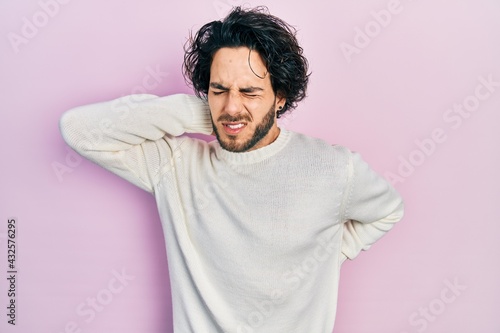 Handsome hispanic man wearing casual white sweater suffering of neck ache injury, touching neck with hand, muscular pain